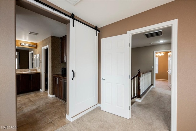 hallway with light colored carpet, a barn door, and sink