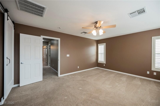 unfurnished bedroom featuring a barn door, light carpet, and ceiling fan