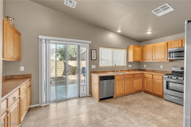 kitchen with vaulted ceiling, appliances with stainless steel finishes, sink, light tile patterned floors, and light brown cabinets