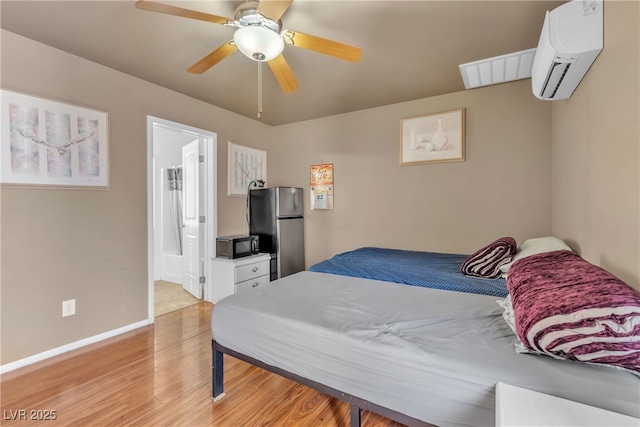 bedroom with light hardwood / wood-style flooring, stainless steel fridge, ceiling fan, a wall mounted AC, and ensuite bathroom