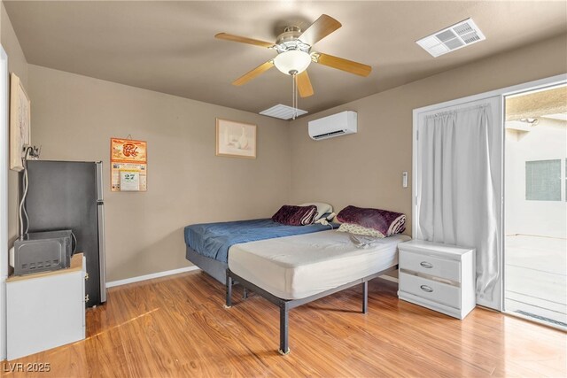 bedroom featuring stainless steel refrigerator, ceiling fan, a wall unit AC, and light hardwood / wood-style flooring