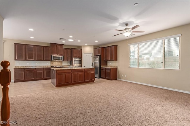 kitchen with decorative backsplash, appliances with stainless steel finishes, open floor plan, light carpet, and baseboards