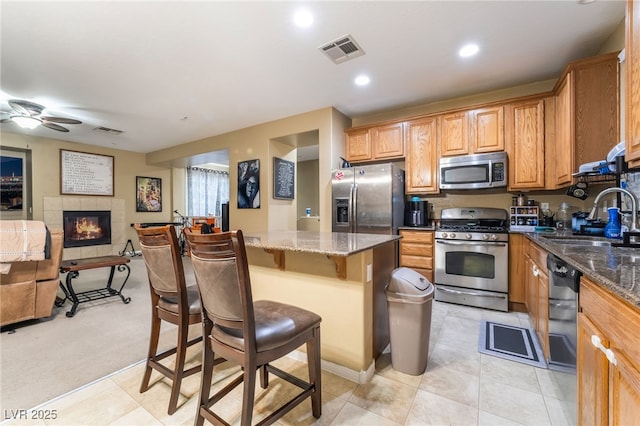 kitchen with sink, stainless steel appliances, a center island, a kitchen bar, and dark stone counters