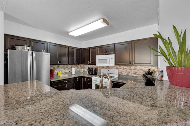 kitchen featuring light stone counters, white appliances, dark brown cabinets, and tasteful backsplash