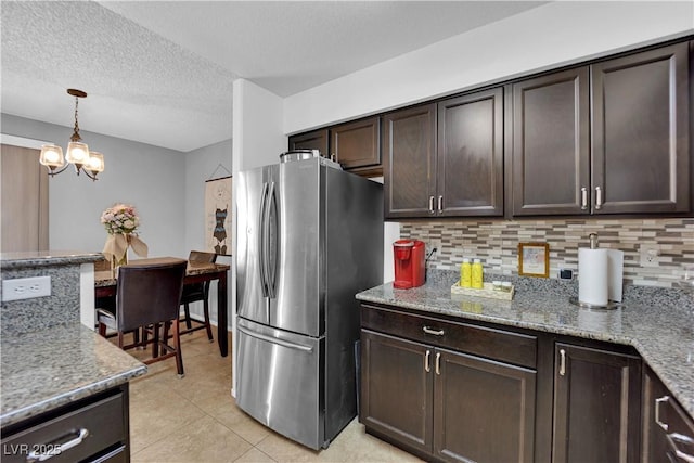 kitchen with light stone counters, pendant lighting, dark brown cabinets, and stainless steel refrigerator