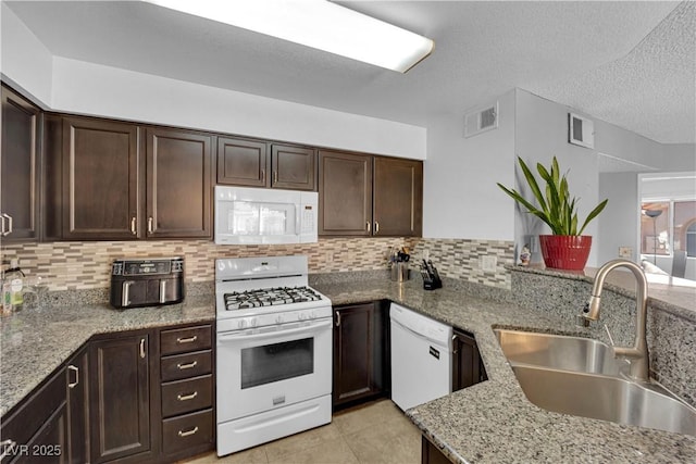 kitchen with light stone counters, sink, white appliances, and kitchen peninsula