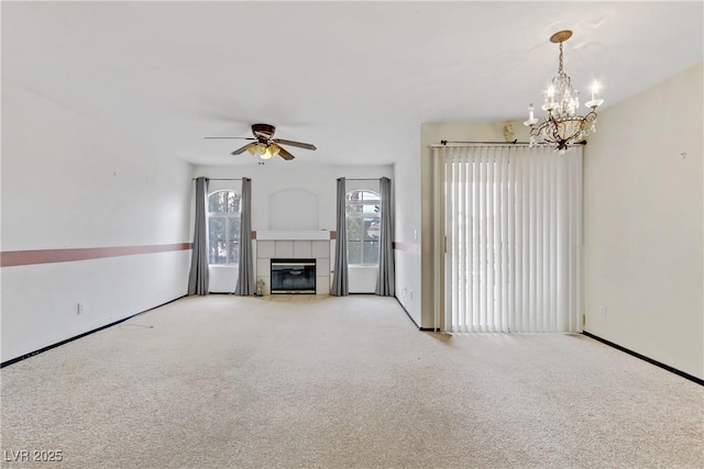 unfurnished living room with a tiled fireplace, ceiling fan with notable chandelier, and light carpet