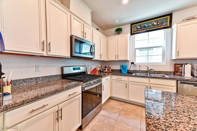 kitchen with appliances with stainless steel finishes, sink, light tile patterned floors, and dark stone counters