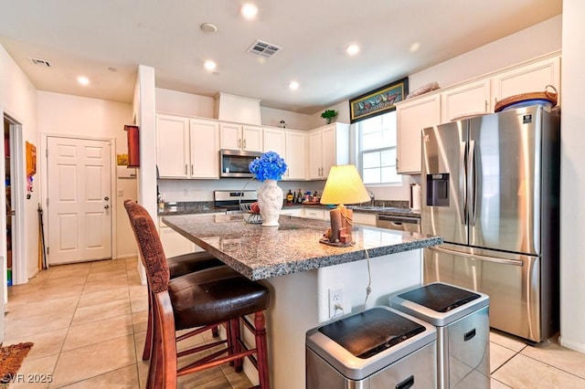 kitchen with white cabinetry, a center island, light tile patterned floors, dark stone countertops, and stainless steel appliances