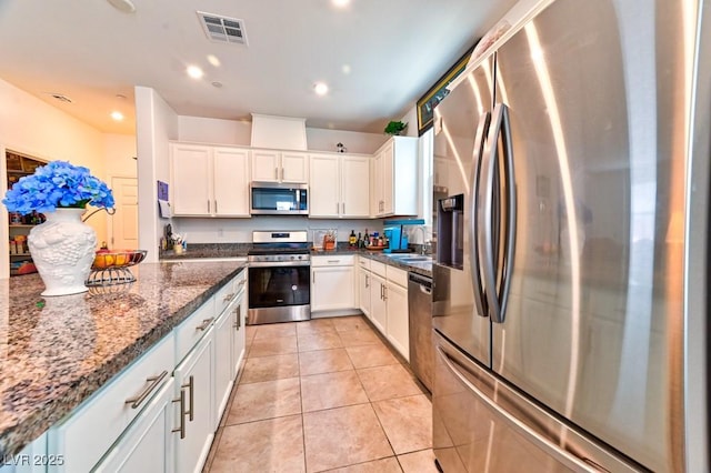 kitchen featuring appliances with stainless steel finishes, white cabinetry, sink, dark stone counters, and light tile patterned floors