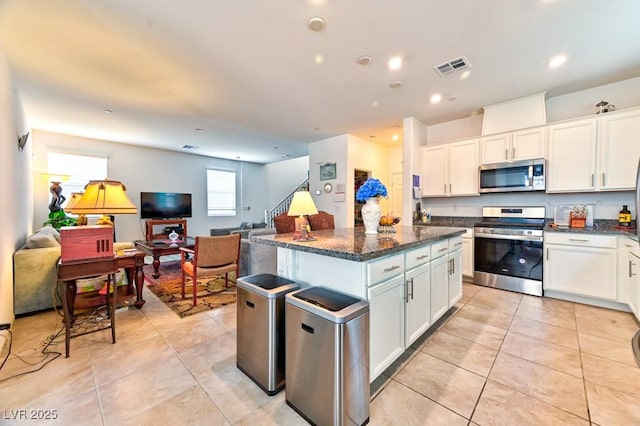 kitchen featuring light tile patterned floors, appliances with stainless steel finishes, dark stone countertops, white cabinets, and a kitchen island