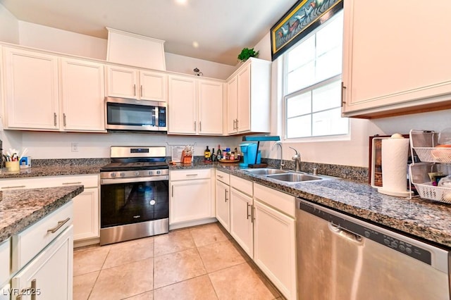 kitchen featuring sink, white cabinetry, dark stone countertops, light tile patterned floors, and appliances with stainless steel finishes