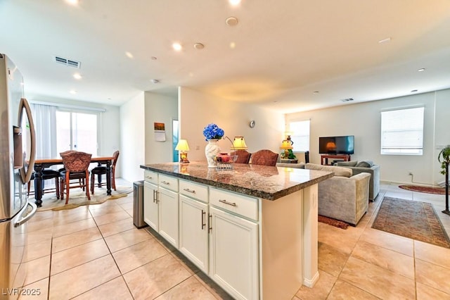 kitchen featuring dark stone countertops, stainless steel fridge with ice dispenser, light tile patterned floors, and a kitchen island