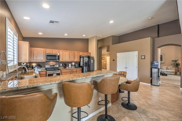 kitchen featuring sink, stainless steel appliances, light stone countertops, and a kitchen bar