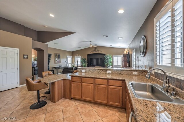 kitchen with a breakfast bar, lofted ceiling, sink, light tile patterned floors, and light stone counters