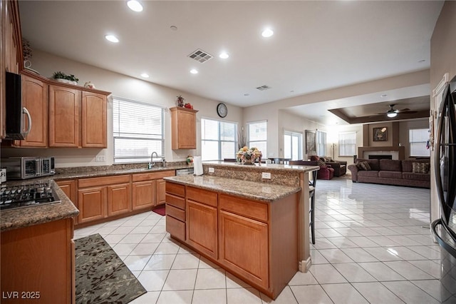 kitchen featuring light tile patterned flooring, stainless steel appliances, a center island, and stone counters