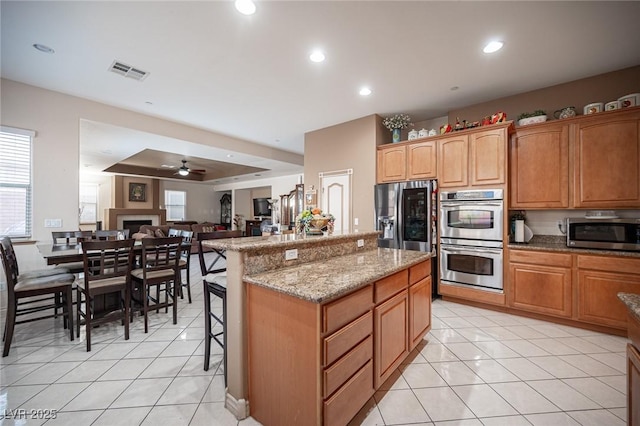 kitchen with appliances with stainless steel finishes, a kitchen breakfast bar, a center island, light stone countertops, and light tile patterned flooring