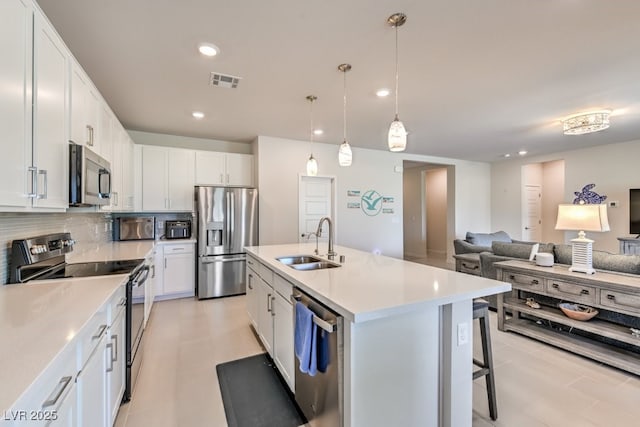 kitchen featuring appliances with stainless steel finishes, decorative light fixtures, white cabinetry, sink, and a center island with sink