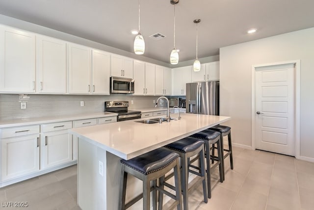 kitchen featuring a kitchen bar, sink, appliances with stainless steel finishes, a kitchen island with sink, and white cabinets