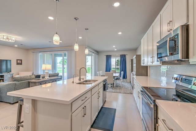 kitchen featuring sink, white cabinetry, stainless steel appliances, an island with sink, and decorative light fixtures