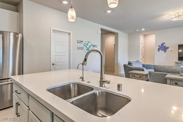 kitchen with white cabinets, sink, pendant lighting, and stainless steel fridge