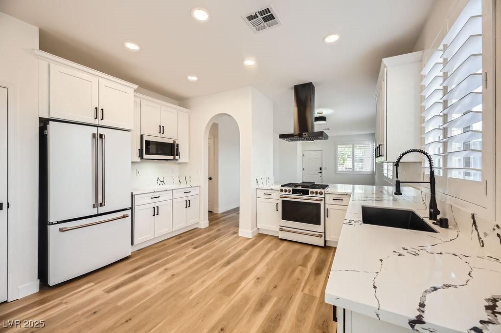 kitchen featuring white appliances, sink, island exhaust hood, white cabinetry, and light stone countertops