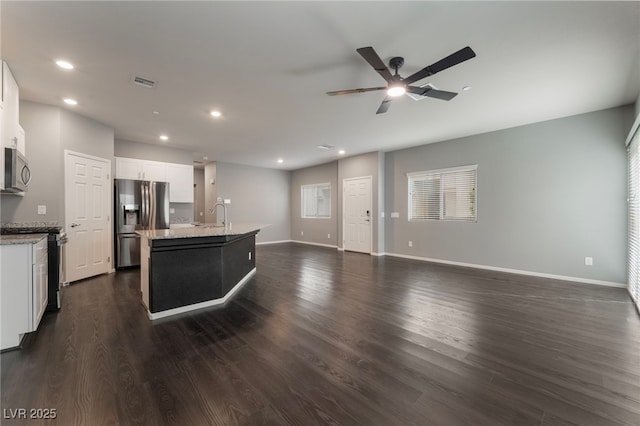 kitchen with stainless steel appliances, light stone countertops, a center island with sink, and white cabinets