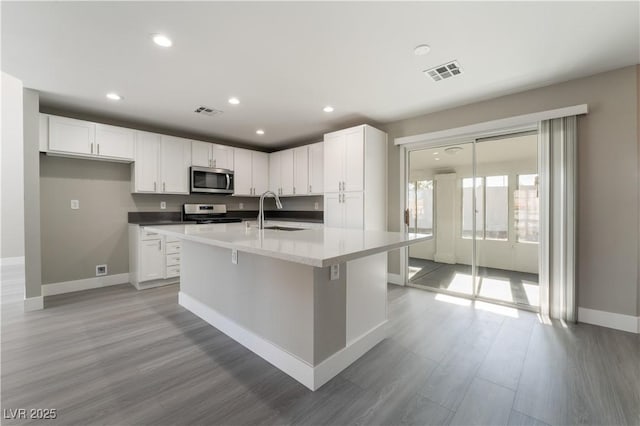 kitchen featuring sink, light hardwood / wood-style flooring, white cabinetry, stainless steel appliances, and an island with sink