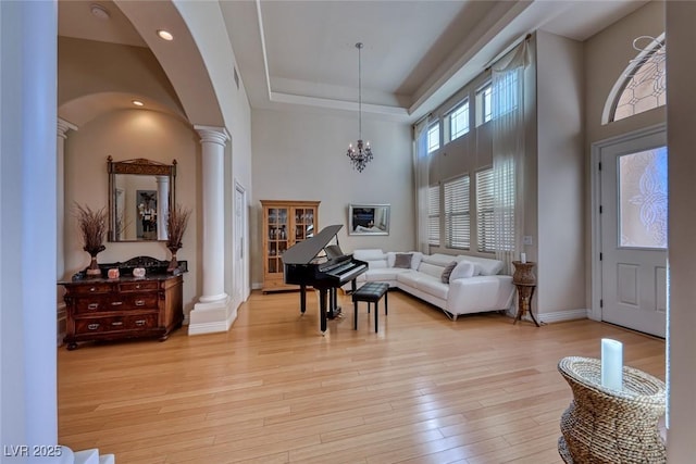 entryway featuring light hardwood / wood-style flooring, a raised ceiling, a high ceiling, and ornate columns