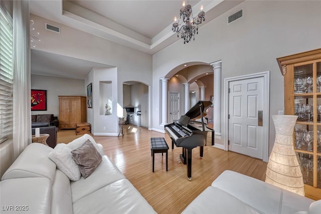 living room with an inviting chandelier, ornate columns, a high ceiling, a tray ceiling, and light wood-type flooring