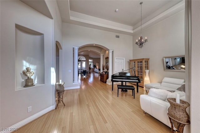 sitting room featuring a towering ceiling, decorative columns, a raised ceiling, an inviting chandelier, and light hardwood / wood-style flooring