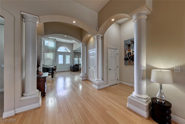 entrance foyer featuring a towering ceiling, decorative columns, and light wood-type flooring