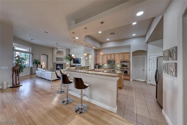 kitchen with a breakfast bar, hanging light fixtures, stainless steel appliances, light stone countertops, and decorative backsplash