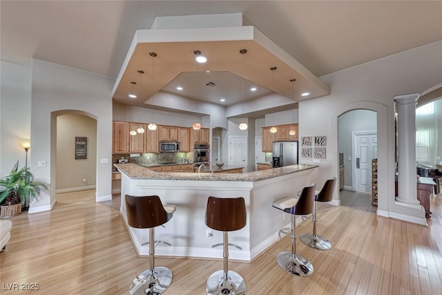 kitchen with pendant lighting, a breakfast bar, appliances with stainless steel finishes, light stone countertops, and kitchen peninsula