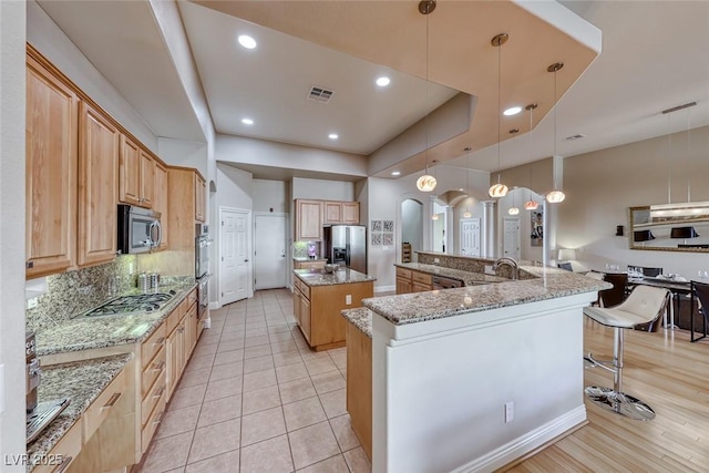 kitchen featuring pendant lighting, a breakfast bar area, appliances with stainless steel finishes, light stone countertops, and a center island with sink