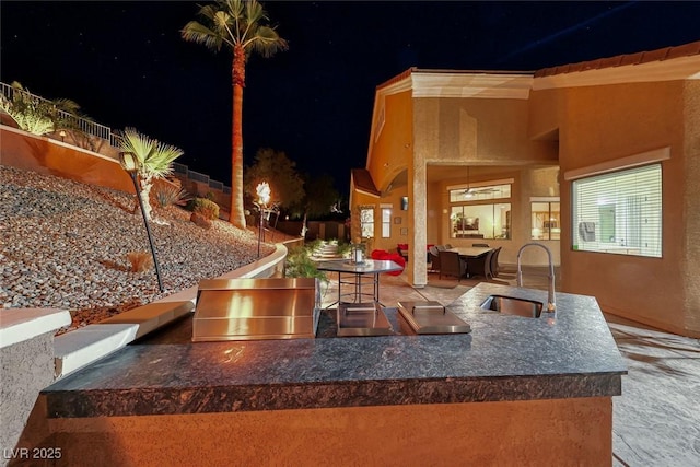 patio at night featuring area for grilling, exterior kitchen, and a wet bar