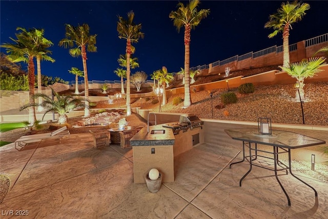 patio at twilight featuring area for grilling, an outdoor fire pit, and an outdoor kitchen