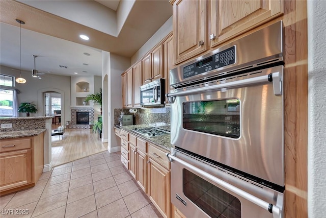 kitchen with light tile patterned floors, stainless steel appliances, light stone countertops, light brown cabinetry, and decorative backsplash