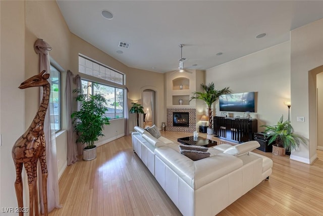 living room with a tile fireplace, ceiling fan, and light wood-type flooring