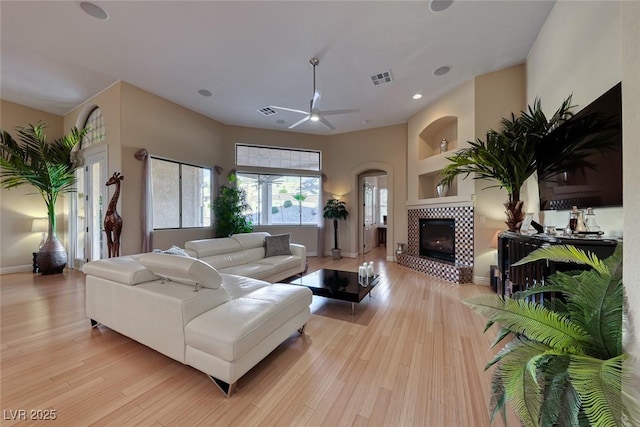 living room with built in shelves, a fireplace, ceiling fan, and light wood-type flooring