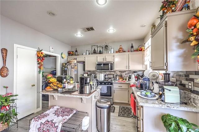 kitchen with appliances with stainless steel finishes, a breakfast bar, backsplash, and light stone counters