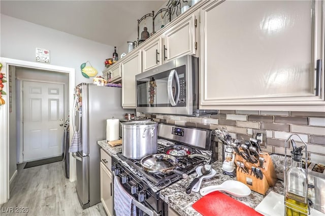 kitchen with appliances with stainless steel finishes, backsplash, light stone counters, and light hardwood / wood-style flooring