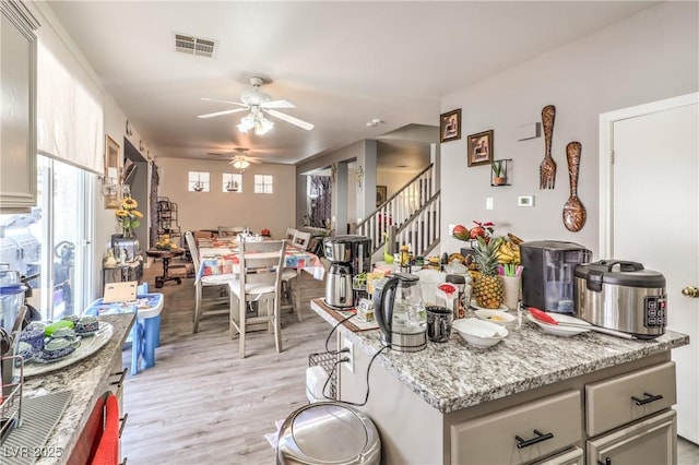 kitchen with light stone counters, ceiling fan, and light hardwood / wood-style flooring