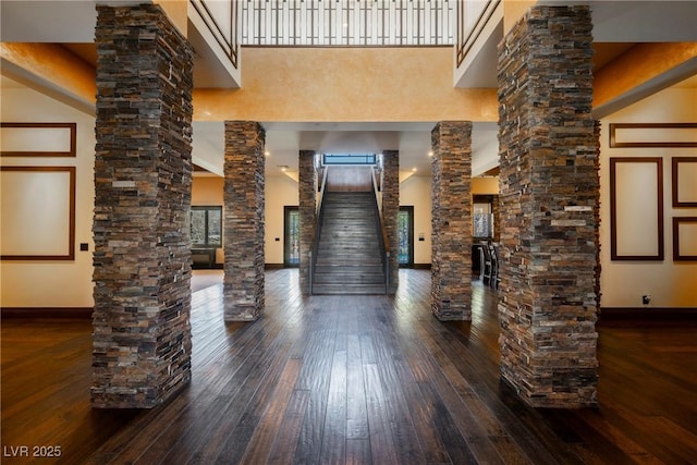 interior space with hardwood / wood-style flooring, decorative columns, baseboards, and a towering ceiling