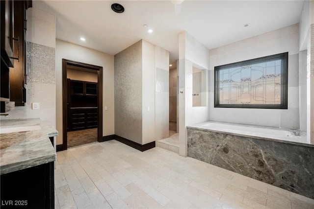 bathroom featuring vanity, baseboards, recessed lighting, a walk in closet, and a garden tub