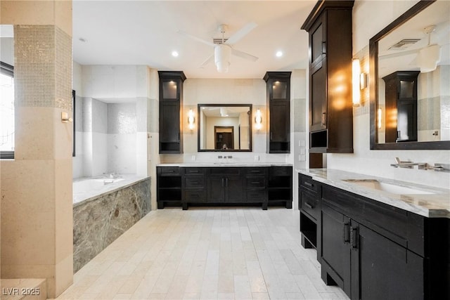 bathroom featuring visible vents, ceiling fan, a garden tub, two vanities, and a sink