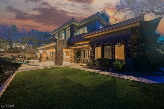 rear view of property featuring stucco siding, stone siding, a yard, a balcony, and a patio area