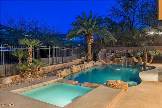 pool at twilight with a pool with connected hot tub, a water slide, and fence