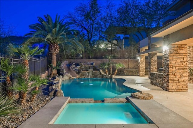 pool at twilight with a patio area, a pool with connected hot tub, and a fenced backyard