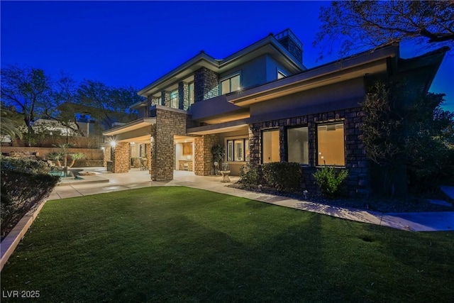 back of house at twilight featuring a lawn, stucco siding, a balcony, stone siding, and a patio